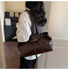 Detail of dark brown glossy tote bag with silver buckle and elegant side-carry look