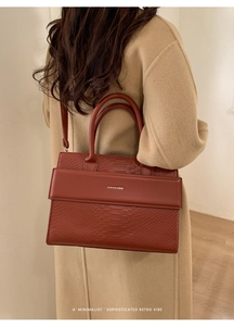 Detailed side view of brick red snake pattern tote bag styled with a beige wool coat