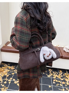 Detail of a brown suede handbag with metal buckle and a white plush rabbit charm