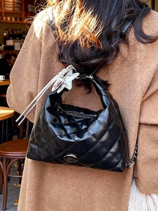 Quilted black leather half-moon tote bag with star charm on a woman in a camel coat
