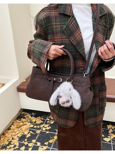 Detail of dark brown faux suede handbag with a cute white bunny charm and buckled strap