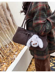 Detail of dark brown leather handbag with buckle decoration and plush rabbit charm