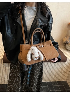 Brown suede handbag featuring leather strap details and a plush rabbit charm accessory