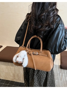 Brown suede tote bag with decorative straps and a plush bunny charm on a model
