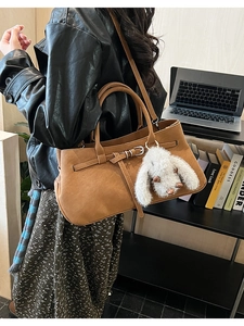Detail of tan tote bag featuring lychee grain texture, metal buckle, and rabbit charm