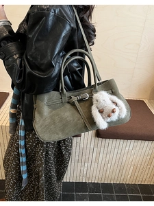 Close-up of olive green suede handbag with leather strap and plush bunny charm