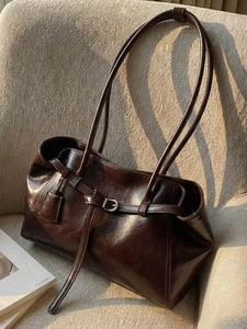 Retro dark brown leather tote bag with buckle detail on a textured chair in natural light