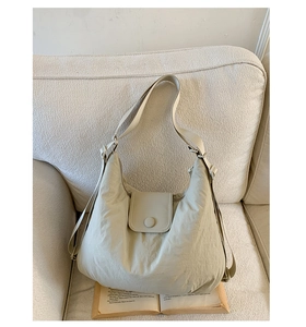 Detail of light beige hobo tote bag in wrinkled nylon on cream sofa with book