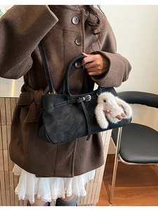 Detail of black vintage leather handbag with plush rabbit charm worn on a wool coat
