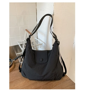 Detail of a black quilted tote bag with flap closure and round button on a wooden surface