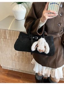 Detail of matte black tote bag with strap buckle and white bunny charm on a wool coat