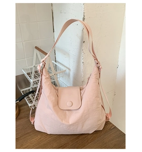 Light pink nylon hobo bag featuring a semi-moon shape and wide strap in a minimalist setting
