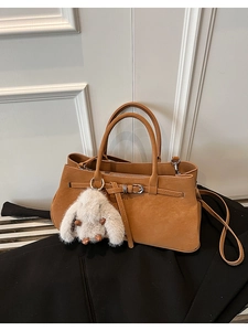 Detail of camel matte leather handbag featuring metal buckle and plush rabbit charm accessory