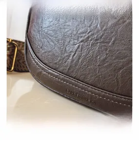 Détail du sac en cuir grainé marron foncé avec logo embossé et bandoulière tissée