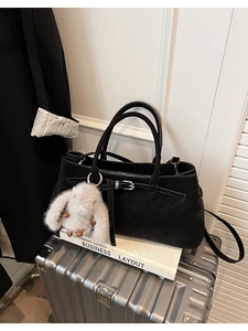 Detail of black leather tote bag with decorative buckle and plush rabbit charm on a suitcase