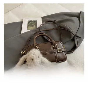 Detail of a brown leather Boston bag with white stitching and a plush rabbit charm