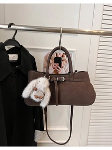 Detail of deep brown leather shoulder bag featuring a cute white rabbit plush charm