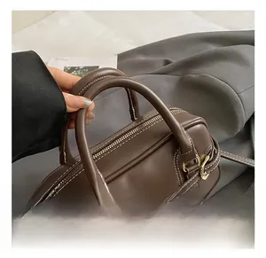 Detail of coffee brown leather boston bag showing white contrast stitching and gold hardware