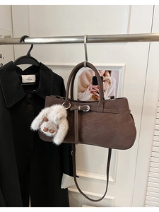Detail of a brown PU leather handbag featuring decorative buckle and plush bunny charm