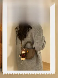 Detailed view of a brown pebbled leather bucket bag with a cute bear charm and gold lock