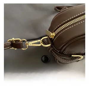 Detailed view of dark brown leather pillow bag with gold metal hooks and white stitching