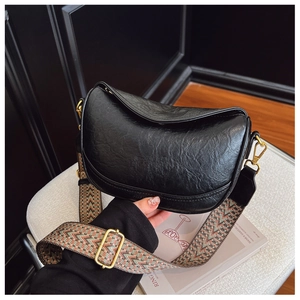 Détail d'un sac oreiller en cuir noir avec une élégante bandoulière large en tissu tissé