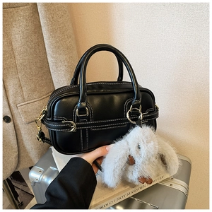 Close-up of black leather Boston bag featuring white contrast stitching and plush bunny charm
