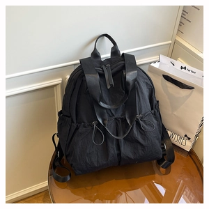 Detailed view of black nylon backpack featuring drawstring flap pockets and wide handle strap