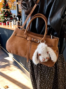 Brown suede handbag with buckle detail and plush bunny charm in festive setting