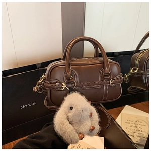 Detail of coffee brown leather Boston bag with white stitching and plush bunny charm