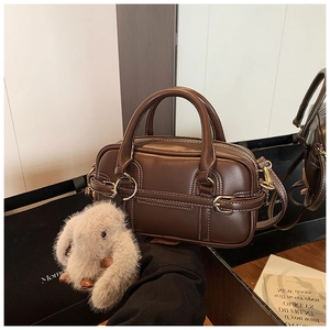 Detail of dark brown Boston bag with contrast stitching and plush rabbit charm accessory