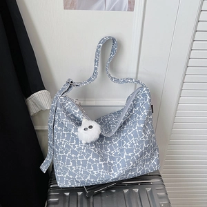 Détail du sac cabas imprimé vache bleu avec pompon en peluche sur une valise argentée