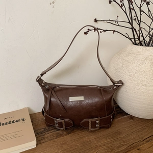 Detail of vintage brown underarm bag with silver plaque and side buckle on wooden surface