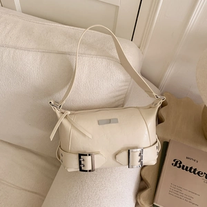 Close-up of beige leather shoulder bag with metallic buckles on a textured fabric sofa