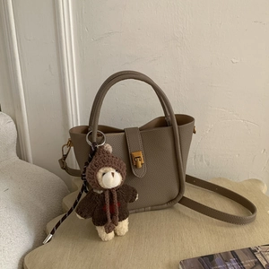 Close-up of taupe litchi grain leather bucket bag with gold clasp and teddy bear charm