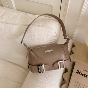 Close-up of taupe leather shoulder bag with vintage silver buckles on creamy sofa