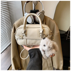Detail of a beige Boston bag with a plush rabbit charm and elegant gold hardware