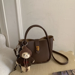 Detail of dark brown pebble leather tote bag with gold buckle and teddy bear charm