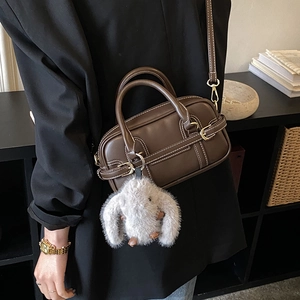 Detail of a dark brown retro Boston bag with contrast stitching and a plush bunny charm