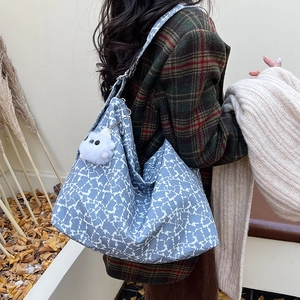 Détail du sac cabas imprimé bleu et blanc avec un charme de monstre en peluche blanc