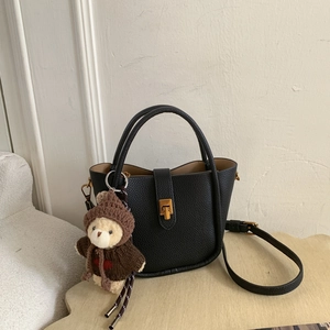 Detail of black lychee grain leather bucket bag with gold hardware and teddy bear charm