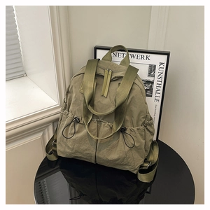 Olive green nylon backpack with drawstring pockets and double zipper on a glossy table