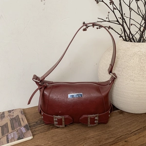 Deep red faux leather shoulder bag with metallic plaque and buckle detail on wood