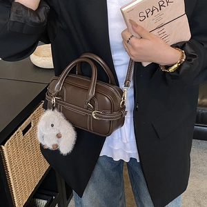 Detail of a brown leather Boston bag with white stitching and a plush charm on the strap