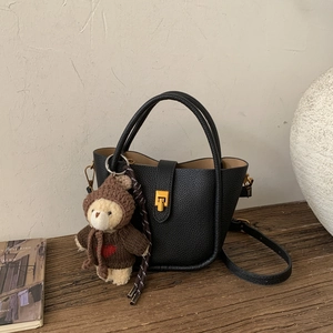 Détail du sac seau en cuir noir avec fermoir doré rotatif et petit charm d'ours