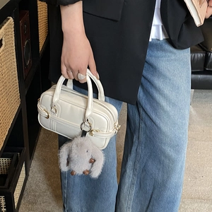 Cream-white Boston bag detail with gray plush rabbit charm held by a model