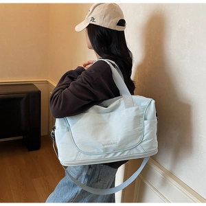 Detail of light blue travel bag with embroidery and adjustable shoulder strap worn by model