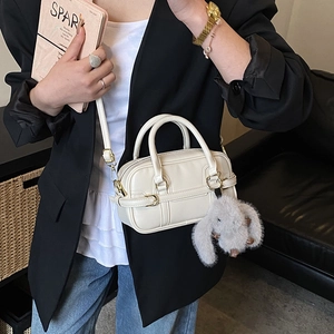 Close-up of off-white faux leather boston bag with detachable strap and plush bunny charm