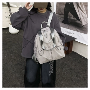 Detail view of the drawstring pleated design and wide silver ribbon strap on the nylon backpack