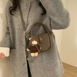 Detail of tan pebble leather bucket bag with a cute plush bear charm on long strap